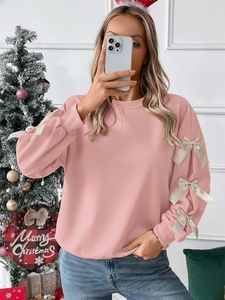 Detail of pink Christmas sweatshirt featuring cream satin bows on sleeves and ribbed cuffs