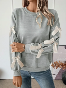Detail showing white ribbon bows on long sleeves of a soft grey crewneck sweatshirt