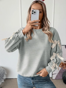 Detail of grey crewneck sweatshirt featuring elegant cream satin bow accents on sleeves