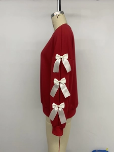 Detail of red crewneck sweatshirt featuring white satin bows on the long sleeves