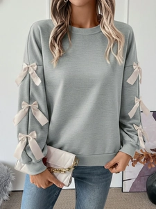 Detail of grey-green long sleeve sweatshirt featuring white satin bows on the sleeves