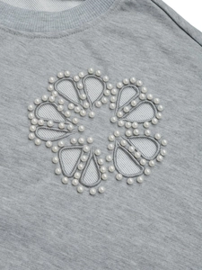 Dettaglio dell'elegante ricamo floreale con perle bianche su una felpa grigia in maglia