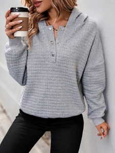 Detail of grey quilted textured hoodie showing metal button half-placket and ribbed cuffs