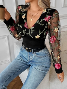 Detailed view of intricate floral embroidery and lace sleeves on a black V-neck top