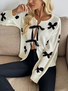 Détail d'un cardigan en maille crème avec motifs nœuds noirs et fermeture à nouer