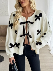 Détail d'un cardigan en maille blanc cassé avec motifs nœuds noirs et rubans à nouer