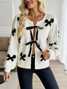 Détail du cardigan en maille crème avec motifs de nœuds noirs et rubans élégants