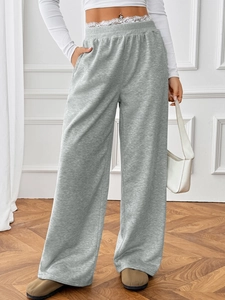 Detail of grey high-waisted wide leg pants featuring elegant white lace trim on the waist