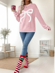 Pink Christmas sweater with white bow detail and contrast knit cuffs in a cozy home setting