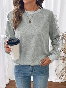 Close-up detail of white lace stitching and bow knots on light gray long sleeve sweatshirt