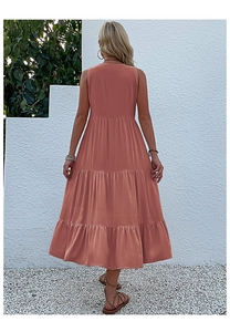 Outdoor back view of a coral tiered sleeveless midi dress against a white textured wall