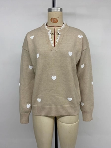 Detailed view of apricot V-neck sweater with white heart jacquard and lace trim
