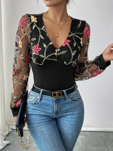 Détail des manches en tulle brodé de fleurs et décolleté en V profond sur body noir