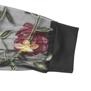 Détail de broderies florales colorées sur une manche en résille noire avec poignet élastique