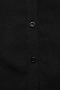 Dettaglio di un abito a camicia nero in tessuto opaco con bottoni in resina tono su tono