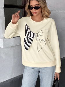 Detail of oversized 3D striped bow and artistic line graphic on a cream sweatshirt