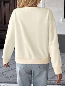 Detail view of cream long sleeve sweatshirt back with ribbed hem and blue denim jeans