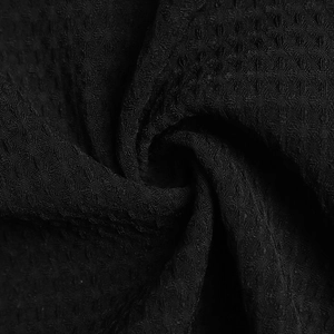 Vue macro du tissu gaufré noir montrant la texture premium et le détail du cardigan