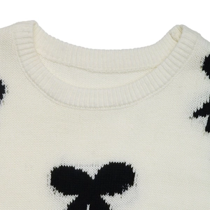 Detail of round neckline with ribbed knit and black bow pattern on cream sweater