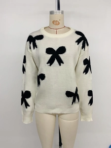 Detail of white knit sweater with black bow patterns and ribbed cuff finishing