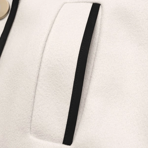 Detail of wool coat pocket with black contrast trim and a round button closure