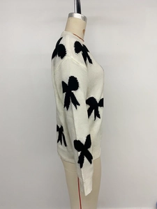 Close-up detail of white knit sweater featuring black bow jacquard patterns and round neck