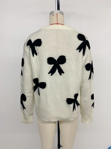 Detail of white crew neck knit sweater featuring black bow jacquard patterns and ribbed hem