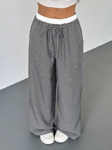 Dettaglio dei pantaloni a gamba larga a righe bianche e nere con vita alta e coulisse regolabile