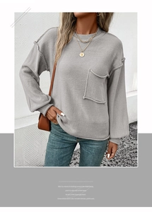 Detail of grey knitted sweater featuring a crew neck and a raw edge front patch pocket