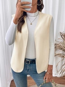 Detail of a minimalist cream fleece vest worn over a white ribbed turtleneck sweater