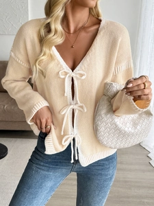 Detail of beige V-neck knit cardigan with white bow tie closures and contrast trim