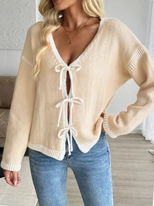 Detail of V-neck knit cardigan featuring elegant white trim and three bow-tie closures
