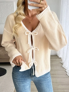 Detail view of cream knit cardigan featuring white ribbon bow ties and ribbed texture