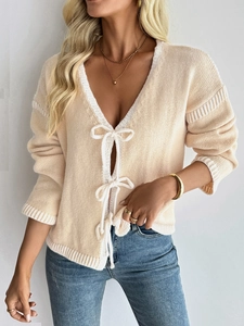 Detail of knit cardigan with V-neck and decorative white ribbon bows closure on the front