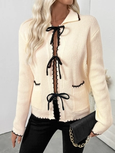 Détail du cardigan en maille crème avec nœuds noirs et coutures contrastées