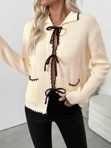 Détail du cardigan en maille crème avec surpiqûres contrastées et nœuds marron