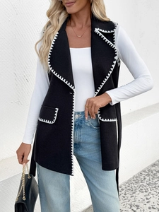 Détail de la couture en zigzag blanche sur le col et la poche d'un gilet noir long