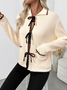Détail du cardigan en maille crème avec surpiqûres marron et fermetures à nœud papillon