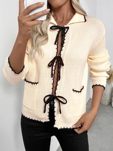Détail du cardigan en maille côtelée crème avec nœuds noirs et coutures contrastées