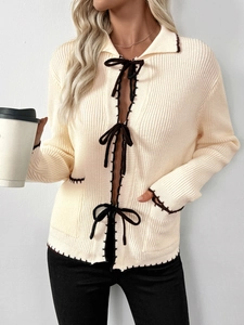 Détail du cardigan en maille crème avec nœuds marron et bordures festonnées