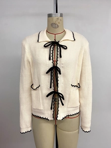 Détail du cardigan avec nœuds noirs et bordures contrastées sur tissu de couleur crème
