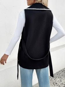 Détail de broderie blanche sur gilet noir avec ceinture de taille réglable assortie