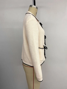 Détail du cardigan en maille avec bordure festonnée noire et nœuds en velours sur la manche