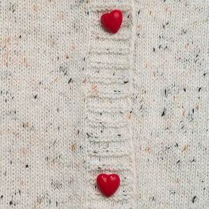 Detail of speckled off-white knit cardigan featuring two red heart-shaped buttons