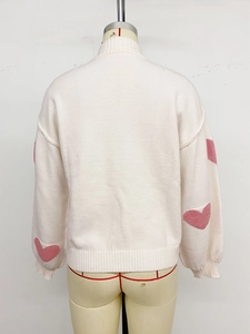 Detail des rosa Herz-Jacquards auf weißem Strickpullover mit gerippten Bündchen