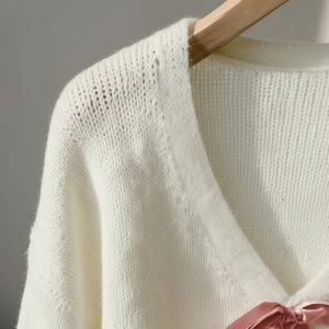 Nahaufnahme eines weißen V-Ausschnitt-Strickpullovers mit rosa Seidenschleifen-Detail