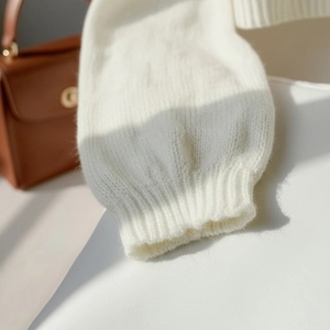 Nahaufnahme der gerippten Bündchen an einem cremefarbenen Strickpullover aus Wolle