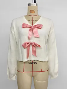 Detail eines weißen V-Ausschnitt-Pullovers mit rosa Satinschleifen und Rippbündchen