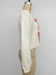 Detail eines weißen Strick-Cardigans mit rosa Seidenschleifen und Rippbündchen an Model