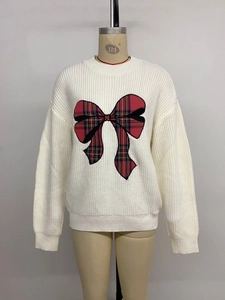Detailed close-up of thick knit white sweater with a red tartan bow embroidery